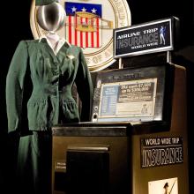 A mannoquin wears a 1950s green flight attendant's uniform next to an airline trip insurance machine.