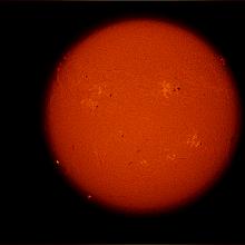 Disk view of the Sun with multiple visible sunspot clusters and prominences of plasma rising above the Sun's surface.