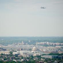 The Space Shuttle Discovery, attached to an aircraft modified for transporting shuttles, flies over the United States Capitol.