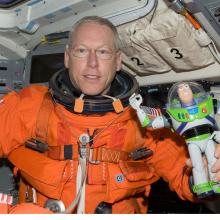 Patrick G. Forrester, an astronaut, holds a Buzz Lightyear figure in his hand while aboard a space shuttle.