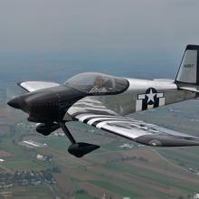 Side view of silver-colored, black, and white aircraft flying in the air with nonretractable landing gear.