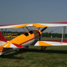 Back view of yellow, red, and white biplane with single engine.