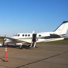 Side view of white aircraft with open door allowing interior access in the middle of the fuselage.