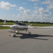 Frontal view of white monoplane with long wings and fixed landing gear.