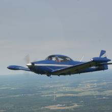 Side view of blue monoplane with a single engine in flight.