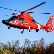 Side view of red helicopter with four blade propellor flying in the air.