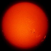 Disk view of the Sun with a large sunspot cluster and a large prominence floating above the surface of the sun.