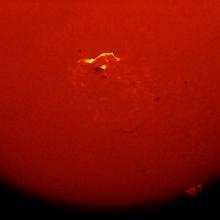 Partial disk view of the Sun focusing on a solar flare, highlighted in yellow with nearby black darkspots, visible from an image of the chromosphere of the Sun.