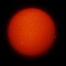 Disk view of the Sun with one visible sunspot cluster, highlighted in a yellow colour, and small prominences floating off the Sun across the bottom half of the visible Sun.