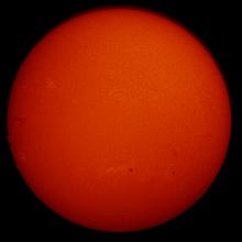 Disk view of the Sun's chromosphere. The left side of the disk features a dark line of gases floating above the Sun's surface known as a filament turn into a prominence as it moves beyond the end of the disk. Multiple sunspots, highlighted as dark marks, and phages, lighter sections, are found throughout the disk.