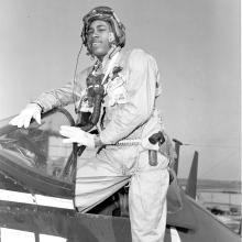 General Frank E. Petersen, an African-American Marines aviator, poses as he steps into a plane. He is wearing pilot gear.