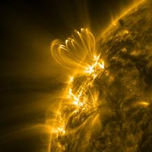 A partial view of the sun focusing on the eruption of a solar flare in bright yellow. The solar flare expands beyond the layer of the sun photographed.