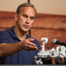 A white man directs his hand towards a Rover model.