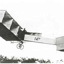 A person flies an early biplane with multiple box-like shapes forming the wings and nose.