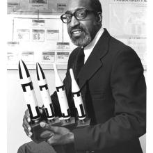 Frank Crossley, an African-American man, sits with a set of trophies featuring rocket figurines.