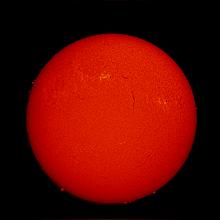 Disk view of the Sun's chromosphere. A few prominences of floating gases are visible on the edges and two sunspot clusters are divided by a filament, or a darker-appearing line of floating gases within the disk.