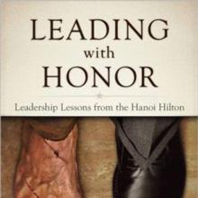 Cover of a book titled "Leading with Honor: Leadership Lessons from the Hanoi Hilton". Below the title is an image of two feet. The right foot is bare without any shoes whereas the left foot is wearing a black dress shoe.