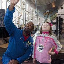 Former Astronaut Leland Melvin, an African-American man, kneels next to a young child at the Museum.