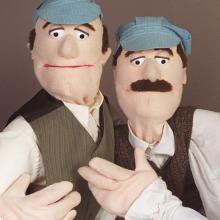 Two puppets dressed as the Wright brothers pose for a portrait.