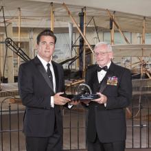 Dr. Adam Steltzner and Gen. Jack Dailey, two white men, pose for a photo as Steltzner accepts a trophy.