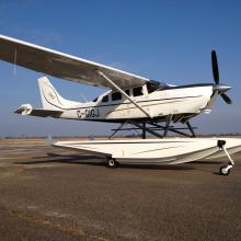 Side view of white amphibian aircraft with fixed floats attached below the cockpit of the aircraft.