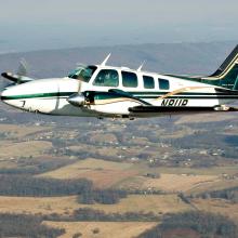 Side view of a white and green monoplane with twin engines in flight. The registration number "N8UR" is painted in a dark color near the rear of the fuselage.