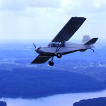 Side view of a white monoplane with one engine in flight. 