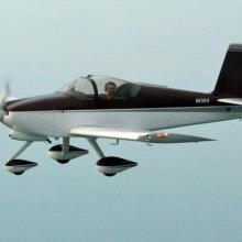 Side view of black and white monoplane in flight with a single engine and fixed landing gear.