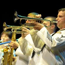 A group of performers in U.S. Navy uniforms play various instruments.