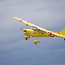 Side view of yellow monoplane in flight with single engine and fixed landing gear.