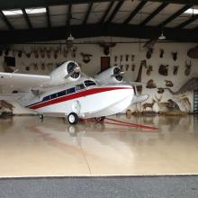 Side view of white and red amphibious aircraft with twin engines and one pontoon on each wing.