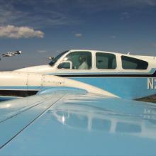 Side view of white and light blue monoplane in flight with twin engines. Registration number "N25JR" is painted in white near the rear of the fuselage.