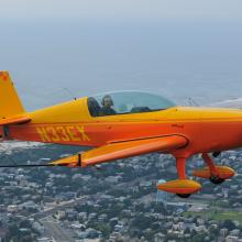 Side view of yellow and orange monoplane with single engine and fixed landing gear. Registration number "N33EX" is painted in yellow behind the cockpit.