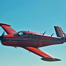 Side view of red and black monoplane in flight with single engine.