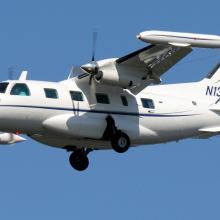 Side view of white monoplane in flight with twin engines. Registration number "N130MS" is painted in blue on the vertical stabilizer.