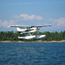 Front view of a white amphibious aircraft with single engine and pontoon floats below the fuselage.