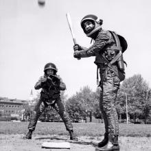 Two people play baseball in suits intended for use in space.