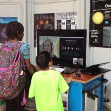 Three museum visitors speak with a museum expert who chats with them through video chat on a computer.