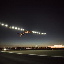 A plane with very long wings lined by lights departs an airport.