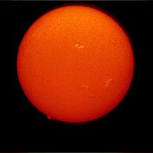 Disk view of the Sun's atmosphere. This image features sunspot clusters (dark spots) surrounded by phages (lighter colored clouds). Filaments (gases floating above the surface) are visible as dark lines on the visible disk, as well as prominences (gases floating from the surface) off the edges of the disk.