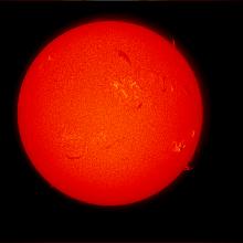 Disk view of the Sun's atmosphere. This image features sunspot clusters (dark spots) surrounded by phages (lighter colored clouds). Filaments (gases floating above the surface) are visible as dark lines throughout the visible disk, as well as prominences (gases floating from the surface) off the edges of the disk on the right side.