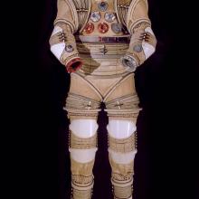 Front view of tan and translucent white full-body experimental spacesuit. Spaces for not present helmet and gloves are open.