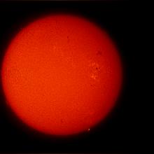 Disk view of the Sun's atmosphere. One sunspot cluster is visible as a dark spot on the Sun surrounded by lighter clouds called phages on the right side of the disk.