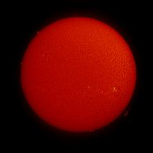 Disk view of the Sun's atmosphere. Two sunspots are visible on the Sun with lighter-colored phages indicating their presence in the bottom right quadrant. A few prominences of red-colored floating gases are visible on the edges across the disk.