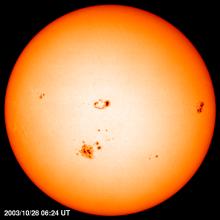 Disk view of the Sun's surface with multiple sunspots and sunspot groups visible as darker spots.