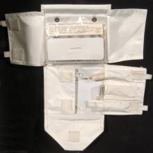 Small maintenance kit made with white fabric and velcro to keep items in place. Multiple items inside small plastic-like bag on upper layer, with three tools visble in a lower section.