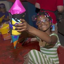 A young girl displays her colorful, finished art project during a family event at the museum.