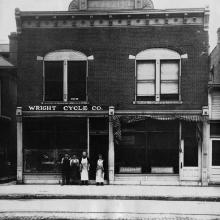 A brick, two-story bulding with a sign on a front facade labeling the building as "The Wright Cycle Co."