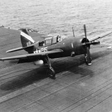 Side view of a monoplane with one engine parked on an naval aircraft hangar. 