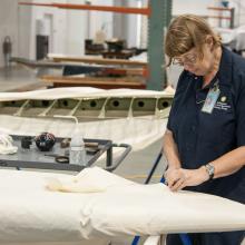 A white female museum specialist performs restoration work involving fabric on the Curtiss Helldiver, an aircraft.